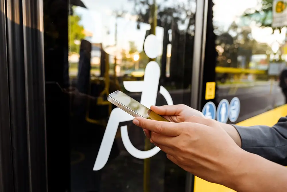 Una persona sostiene su teléfono móvil mientras espera frente a la puerta de un autobús con acceso para personas con discapacidad.