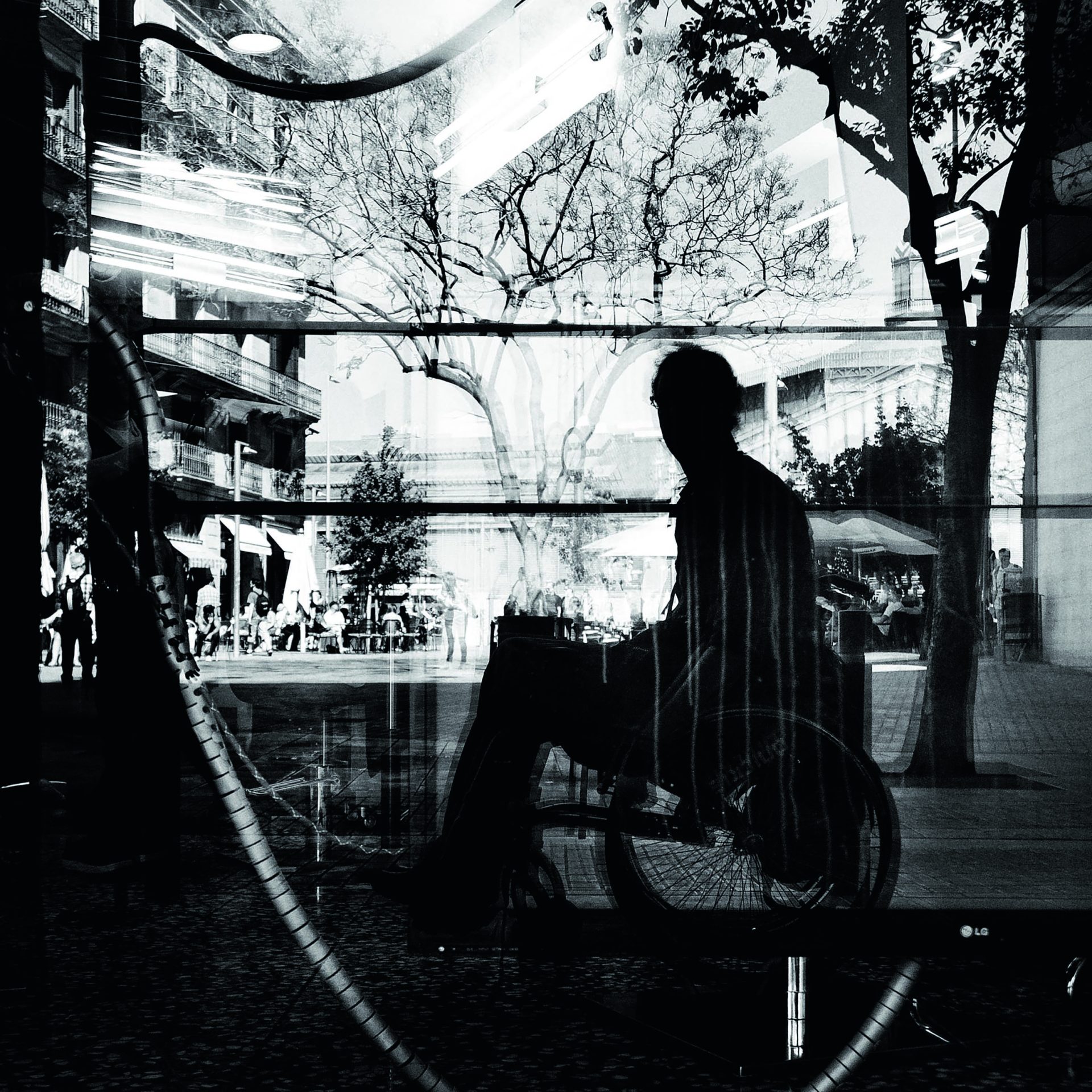Fotografía en blanco y negro de un hombre en silla de ruedas, reflejado en un escaparate