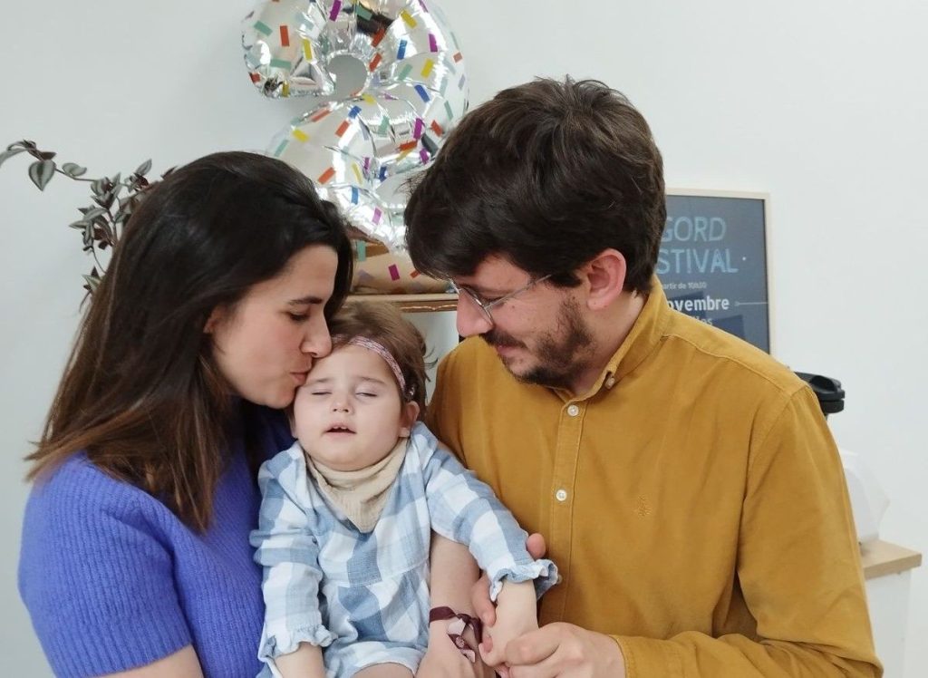 Sobre la imagen una pareja feliz, besando en el moflete a u su hija.