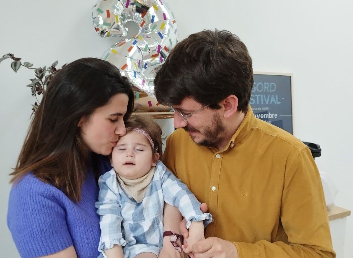 Sobre la imagen una pareja feliz, besando en el moflete a u su hija.