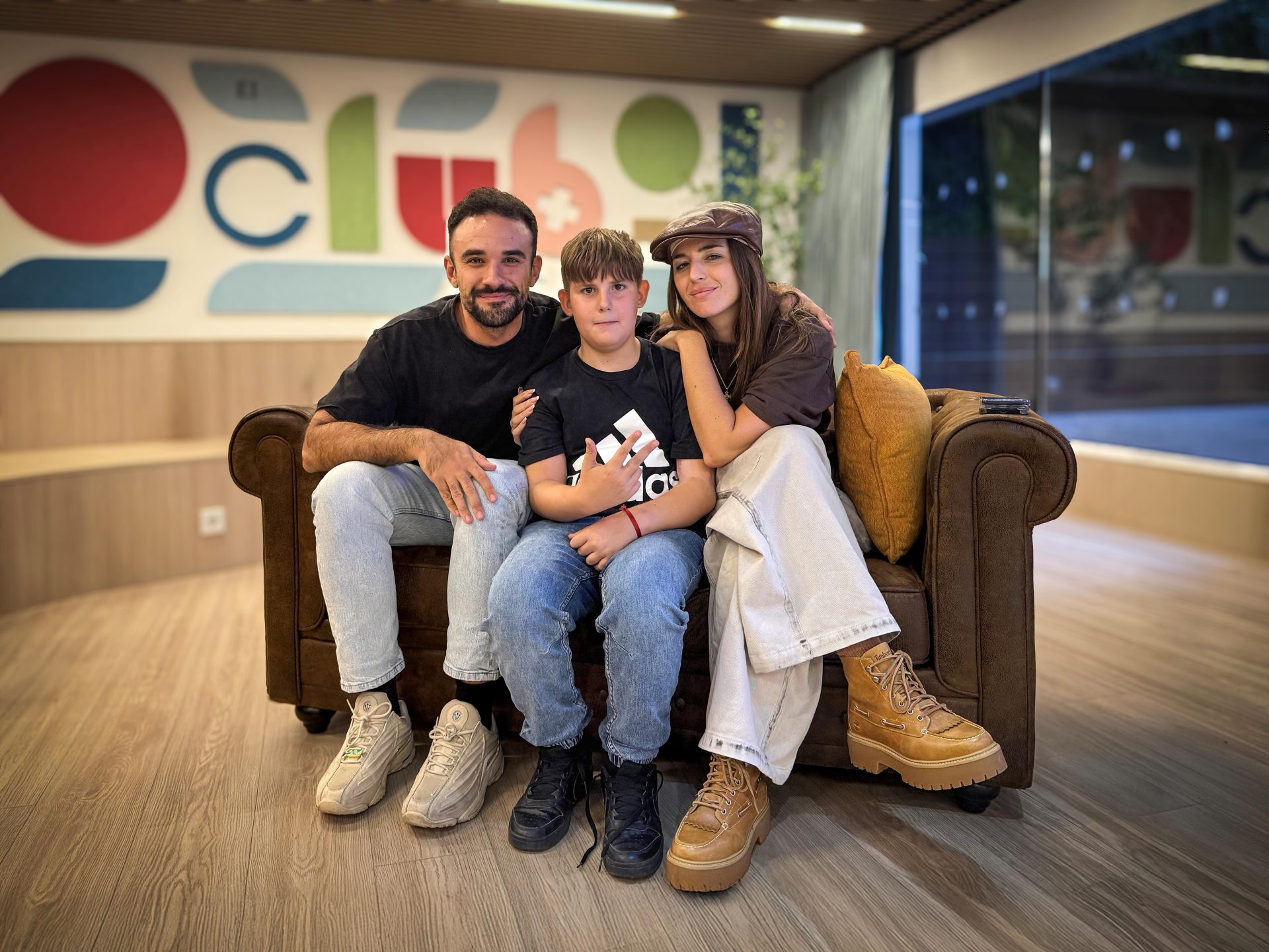 IlloJuan y Lola Índigo con uno de los niños de Fundación Juegaterapia, sentados en un sofá