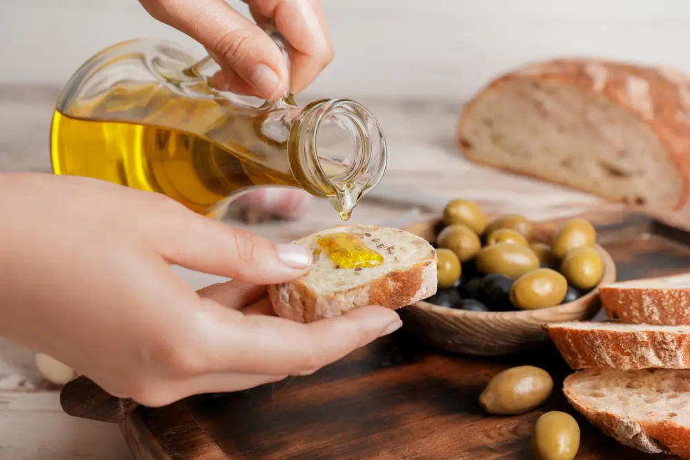 Una rebanada de pan está siendo aliñada con el aceite procedente de una jarrita.