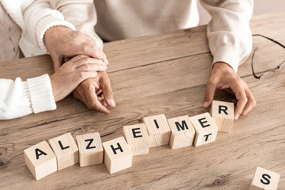 Manos entrelazadas junto a cubos de madera que forman la palabra Alzheimer