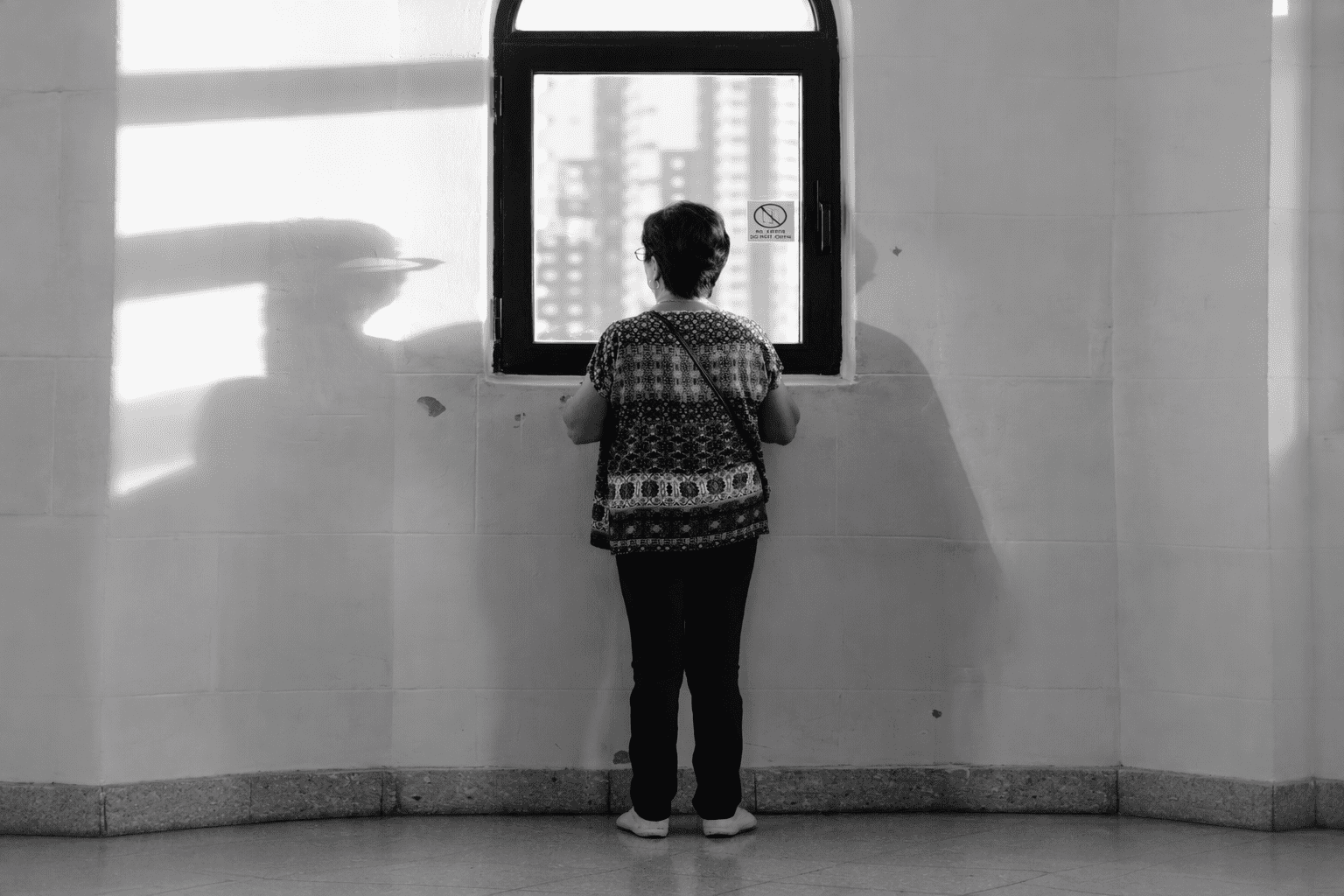 Persona de espaldas frente a una ventana en un espacio interior.