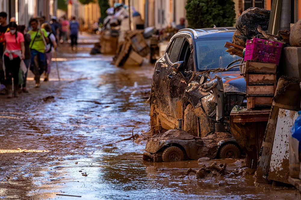 Calle cubierta de barro, con vehículos y enseres dañados tras las inundaciones de la dana en Valencia