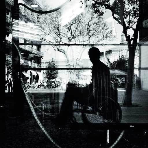 Fotografía en blanco y negro de un hombre en silla de ruedas, reflejado en un escaparate