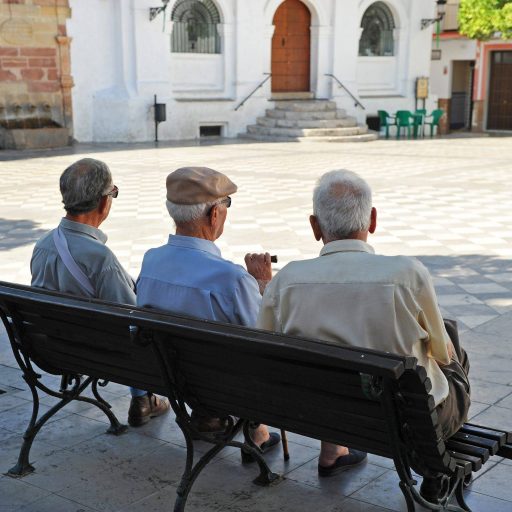 Tres personas mayores sentadas en un banco de lo que parece ser un pueblo rural