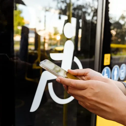 Una persona sostiene su teléfono móvil mientras espera frente a la puerta de un autobús con acceso para personas con discapacidad.